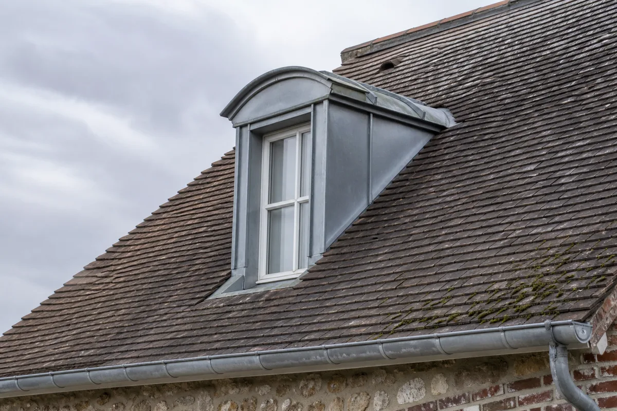 Toiture en tuile plate d’une maison meuliere des Yvelines sous un ciel gris
