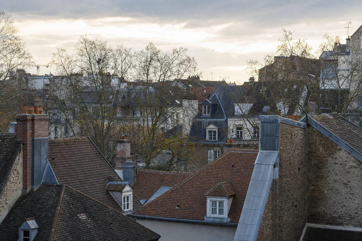 Vue de toits en tuile plate et ardoise d’un centre ancien des Yvelines sous un ciel changeant