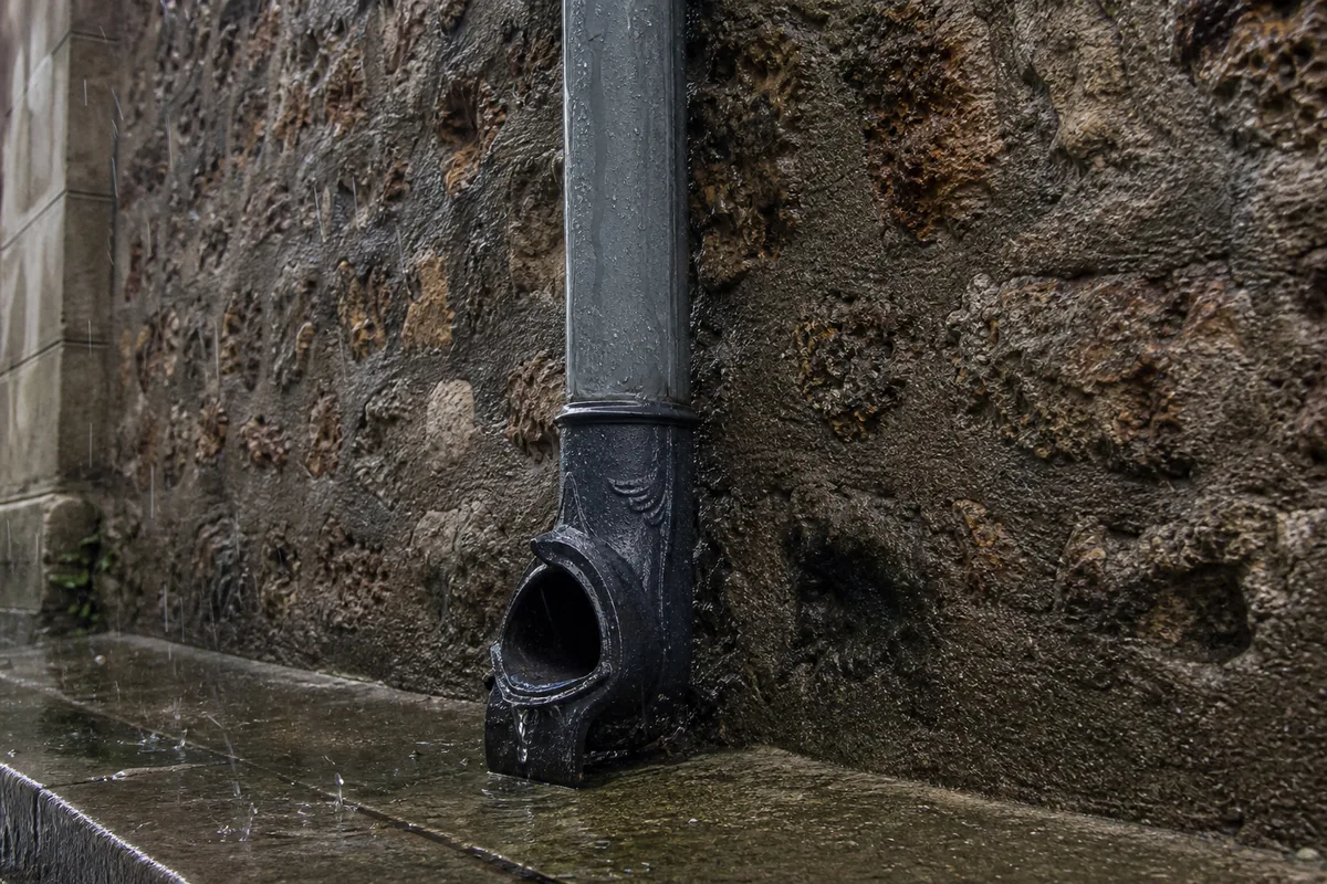 Descente de gouttiere en zinc le long d’une facade de meuliere sous la pluie
